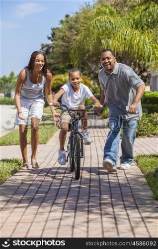 A young African American family with boy child riding his bicycle and his happy excited parents giving encouragement next to him