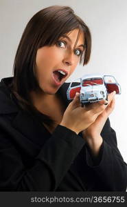 a young and cute brunette looking in camera with surprise and showing a model of an italian car, fiat 600