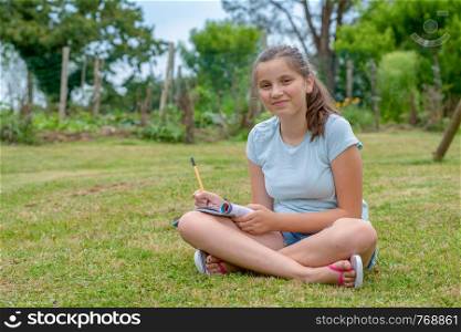a young and smiling teenager sitting cross-legged in the grass