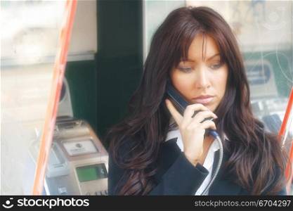 A young and stressed out woman talks on a public phone.