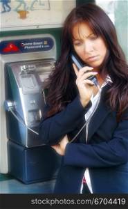 A young and stressed out woman talks on a public phone.