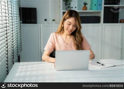 A young Asian female employee sitting at her desk in her office, sitting at desktop in workstation.. A young Asian woman sitting at her desk in her office.