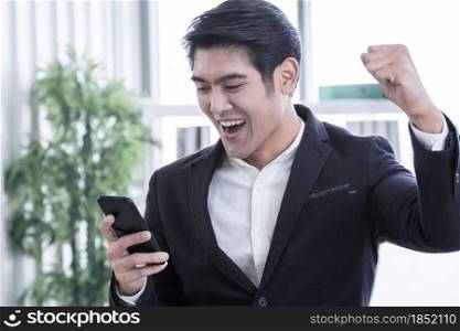 A young asian handsome business man is reading message in mobile phone and celebrating his success