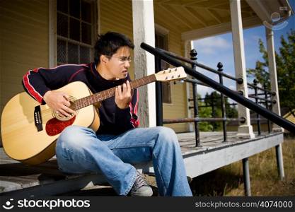 A young asian male playing guitar outside