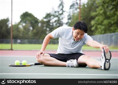A young asian male tennis player stretching before playing