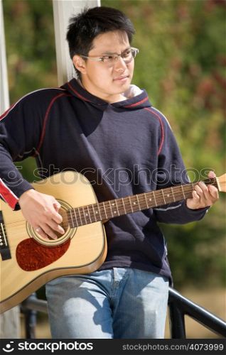 A young asian man playing guitar outdoor