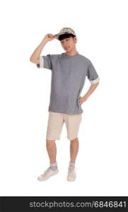 A young Asian teenager standing in shorts an a gray t-shirt with his handon his cap, isolated for white background.