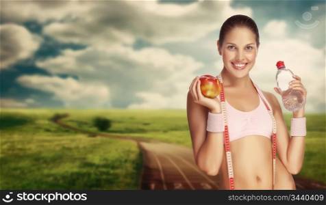 A young athletic woman holding water and apple against running track.