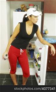 A young Australian woman dressed in her gym gear Drinks water in her kitchen infront of the fridge.