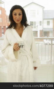 A young Australian woman in her white dressing gown holds a coffee mug in a typical suburban setting at home. Happy and casual