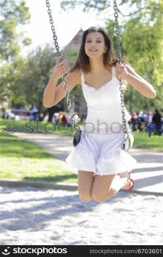 A young Australian woman on a swing in a melbourne park, movement happy smiling.