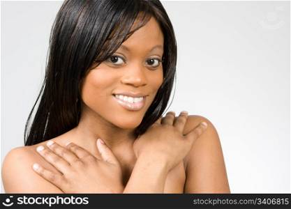 A young bare-shouldered, young African-American woman with her arms across her chest smiles.