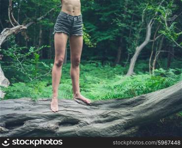 A young barefoot woman is standing on a fallen tree in the forest