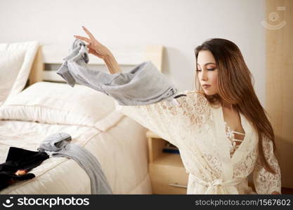 a young beautiful Asian girl in a beige lace nightgown choosing clothes in a wardrobe.