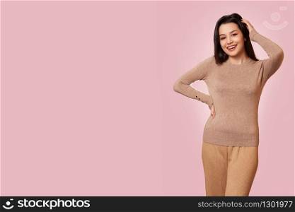 a young beautiful brunette girl in a light brown jacket laughs. on a pink isolated background.
