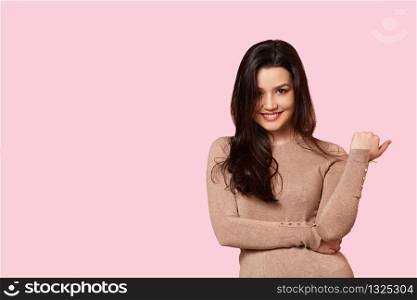 a young beautiful brunette in a light brown sweater is smiling. on a pink isolated background