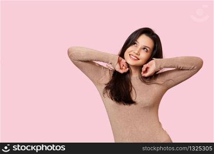a young beautiful brunette in a light brown sweater is smiling. on a pink isolated background