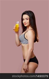 a young beautiful brunette woman in a black swimsuit with fresh juice in her hands on a pink isolated background.