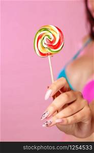 a young beautiful girl holding a colorful bright Lollipop photographed in close-up. on a pink isolated background. with copyspace