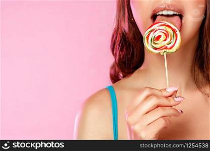 a young beautiful girl licks a colorful bright Lollipop photographed in close-up with her tongue. on a pink isolated background