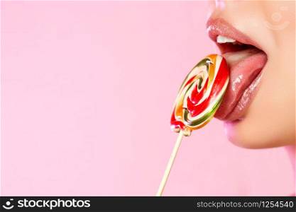 a young beautiful girl licks a colorful bright Lollipop photographed in close-up with her tongue. on a pink isolated background. with copyspace