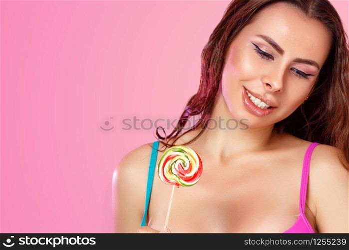 a young beautiful girl with a beautiful body dressed in a swimsuit holds a colorful bright Lollipop. on a pink isolated background. with copyspace