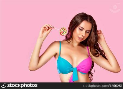 a young beautiful girl with a beautiful body dressed in a swimsuit holds a colorful bright Lollipop. on a pink isolated background. with copyspace