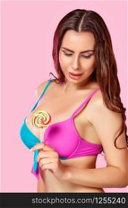 a young beautiful girl with a beautiful body in a swimsuit holds a colorful bright Lollipop. on a pink isolated background. with copyspace