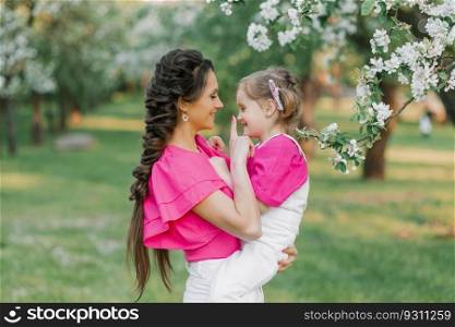 A young beautiful mother is happy and holding her daughter in her arms, they are having fun in the spring park
