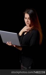 a young beautiful Muslim woman in black clothes uses a laptop . on a black isolated background. vertical framing.
