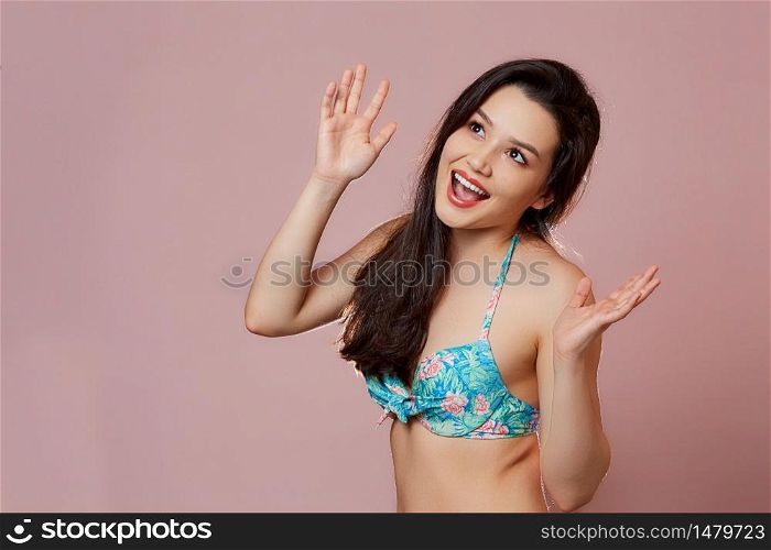 a young beautiful slender Asian girl in a blue swimsuit covered up in surprise, in admiration, in delight . on a pink isolated background.