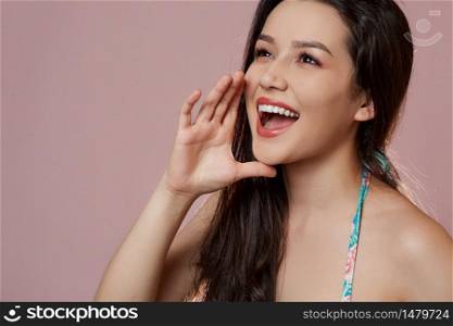 a young beautiful slender Asian girl in a blue swimsuit covered up in surprise, in admiration, in delight . on a pink isolated background.