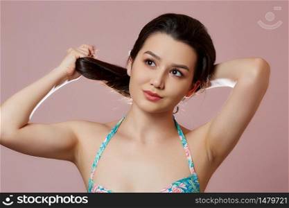 a young beautiful slender Asian girl in a blue swimsuit holds her dark hair. on a pink isolated background