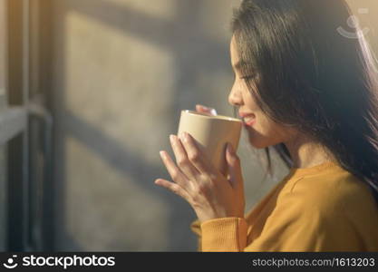 A young beautiful woman in sunshine light enjoying her morning coffee at home.. Young beautiful woman in sunshine light enjoying her morning coffee at home.