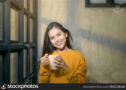 A young beautiful woman in sunshine light enjoying her morning coffee at home.. Young beautiful woman in sunshine light enjoying her morning coffee at home.