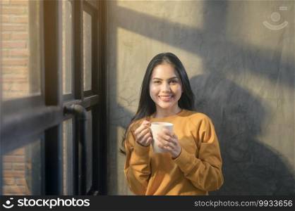 A young beautiful woman in sunshine light enjoying her morning coffee at home.. Young beautiful woman in sunshine light enjoying her morning coffee at home.