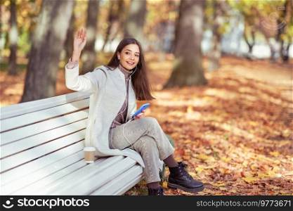 A young beautiful woman is sitting on a bench in an autumn park. A girl listen to music in the autumn forest