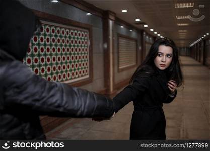 a young beautiful woman tries to escape from a robber in black clothes . in the underpass. at night