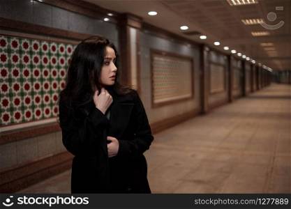 a young beautiful woman walks through an underground passage at night, looking back with fear.