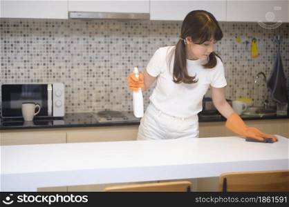 A young beautiful woman wearing protective rubber gloves is cleaning table in kitchen at home.. Young beautiful woman wearing protective rubber gloves is cleaning table in kitchen at home.