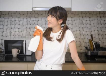 A young beautiful woman wearing protective rubber gloves is cleaning table in kitchen at home.. Young beautiful woman wearing protective rubber gloves is cleaning table in kitchen at home.