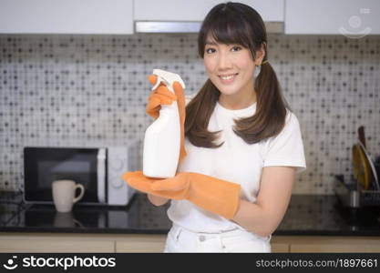 A young beautiful woman wearing protective rubber gloves is cleaning table in kitchen at home.. Young beautiful woman wearing protective rubber gloves is cleaning table in kitchen at home.