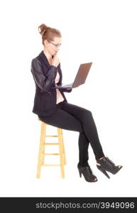 A young blond business woman sitting on a chair working on her laptopin black tights and jacket, isolated for white background.