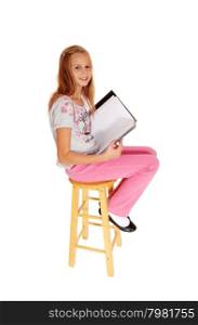 A young blond girl sitting in pink pants, holding her folderand looking into the camera, isolated for white background.