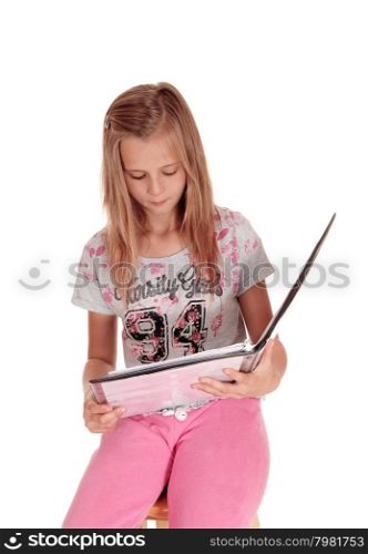 A young blond girl sitting in pink pants, holding her folderand reading from her book, isolated for white background.