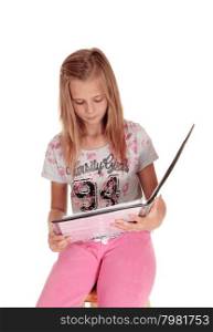 A young blond girl sitting in pink pants, holding her folderand reading from her book, isolated for white background.