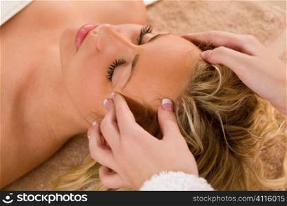 A young blond woman recieving a relaxing head massage from a beauty therapist