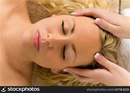 A young blond woman recieving a relaxing head massage from a beauty therapist