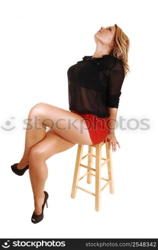 A young blond woman sitting on a chair in red shorts and a black blouselooking up and showing her nice long crossed legs, over white