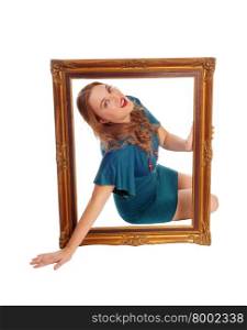 A young blond woman sitting on the floor holding a big picture frameand looking trough, isolated for white background.